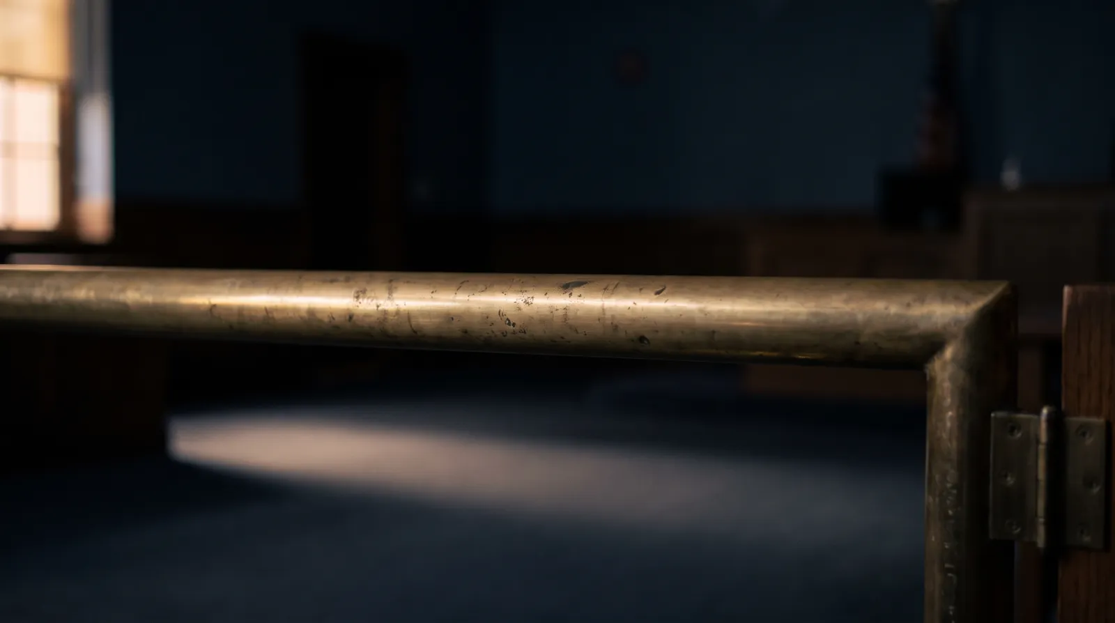 Illustrative detail of a worn brass courtroom rail in dusk window light